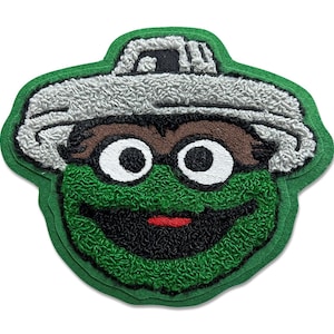 Puede incluir: Parche bordado con la cara de un personaje verde y gruñón con un sombrero de tapa de cubo de basura. El parche tiene un aspecto texturizado, con detalles blancos, marrones, negros y rojos. El parche está contorneado en verde.