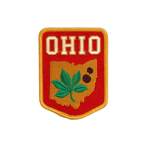 Puede incluir: Un parche bordado rojo y dorado con la palabra "OHIO" en letras blancas y una hoja de buckeye verde sobre un contorno dorado del estado de Ohio.