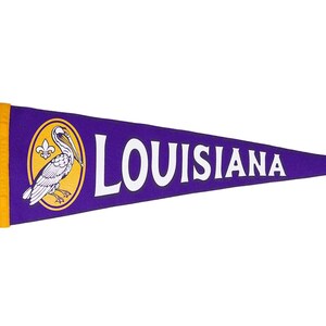 May include: Purple pennant with a white border and yellow fringe. The pennant features a white pelican with a fleur-de-lis on its chest inside a yellow circle. The text "LOUISIANA" is printed in white across the pennant.