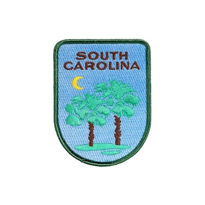 以下が含まれることがあります： 「SOUTH CAROLINA」の文字と、2本のヤシの木と三日月がデザインされた刺繍ワッペン。パッチは青色の背景に緑色の縁取りが施されています。