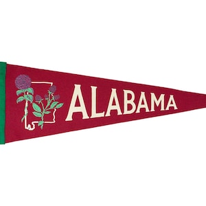 May include: A red felt pennant with white text that reads "ALABAMA". The pennant features a green outline and a white outline of the state of Alabama with a green plant with red flowers inside.