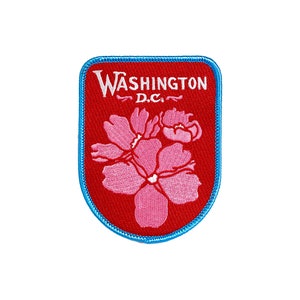May include: Red embroidered patch with a blue border. The patch features a white inscription that reads "WASHINGTON D.C." and a pink embroidered flower.