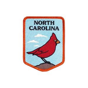 Puede incluir: Un parche bordado azul y naranja con un pájaro cardenal rojo y el texto "NORTH CAROLINA".