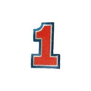 May include: An embroidered patch in the shape of the number one. The numeral features a bright orange centre, a thin white border, and a thick outer border in a medium blue thread. The stitching is dense and uniform throughout the entire design.