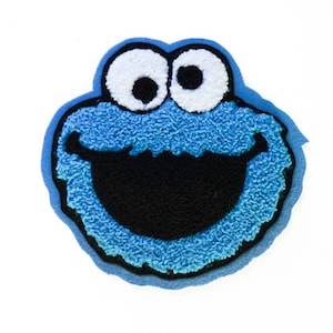 May include: A blue, white, and black Cookie Monster patch. The patch features the character's face with large white eyes, a wide black mouth, and blue fur. The patch has a blue border and is set against a white background.