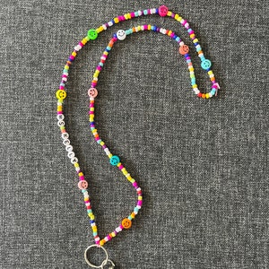May include: A colorful beaded lanyard with smiley face beads and the name "KELLY" spelled out in white letter beads. The lanyard features a silver-colored clasp and key ring.