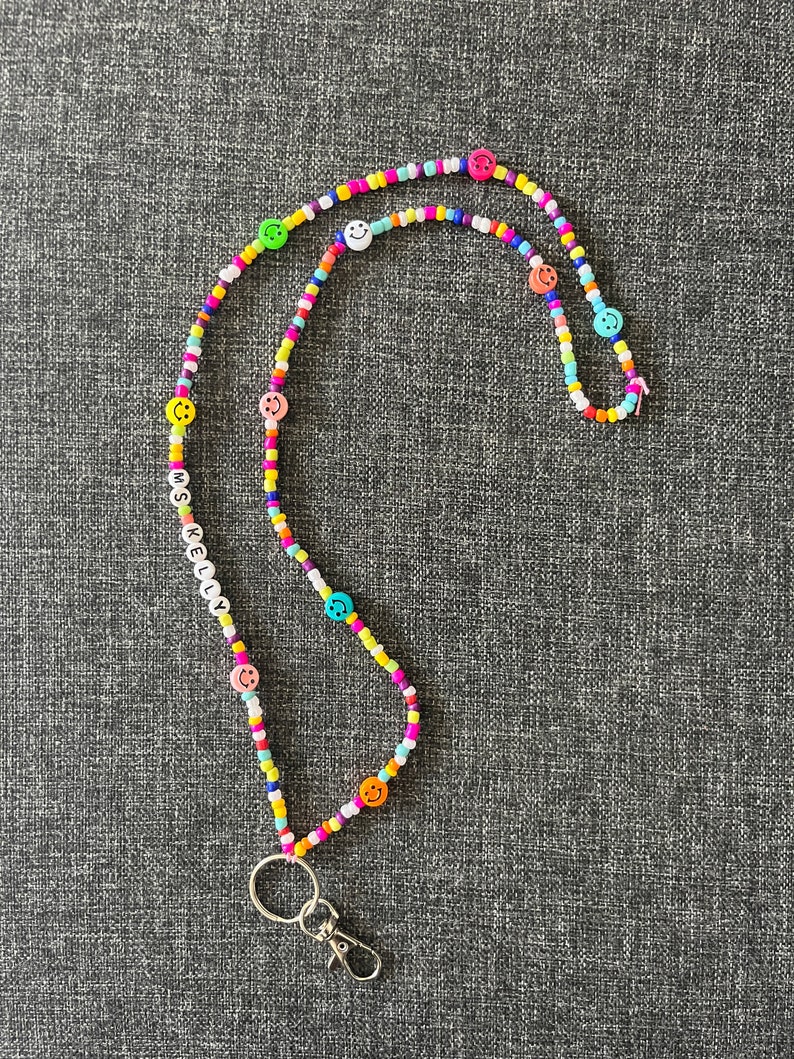 May include: A colorful beaded lanyard with smiley face beads and the name "KELLY" spelled out in white letter beads. The lanyard features a silver-colored clasp and key ring.