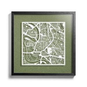 May include: A framed map of Dusseldorf, Germany, with a green background and white lines depicting the city streets. The map is framed in black.