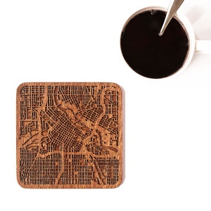 Peut inclure: Un dessous de verre en bois avec un motif de carte de ville découpé au laser. Le dessous de verre est de couleur marron et de forme carrée.