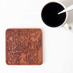 May include: A wooden coaster featuring a detailed laser-cut design of a city map. The coaster is brown and has a square shape.