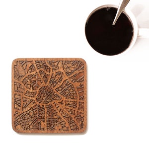 Peut inclure: Un dessous de verre en bois avec un motif de carte de ville découpé au laser. Le dessous de verre est de couleur marron et de forme carrée.