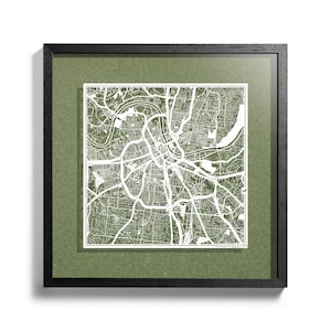 May include: A framed map of Nashville, Tennessee, with a green background and a white paper cutout of the city streets. The map is framed in black.