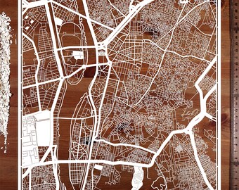 Puede incluir: Un recorte de papel blanco de un mapa de la ciudad, con intrincados detalles de calles y edificios. El mapa se muestra sobre una superficie de madera.