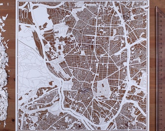 Puede incluir: Un recorte de papel blanco de un mapa de la ciudad con detalles intrincados. El mapa está colocado sobre una superficie de madera.