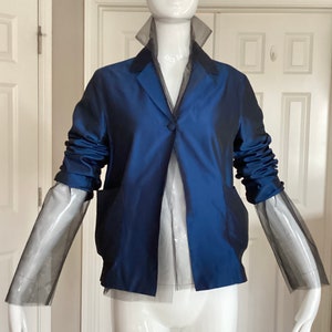 May include: A navy blue blazer with long sleeves and a sheer overlay. The sleeves are gathered at the elbow and the blazer has a single button closure.