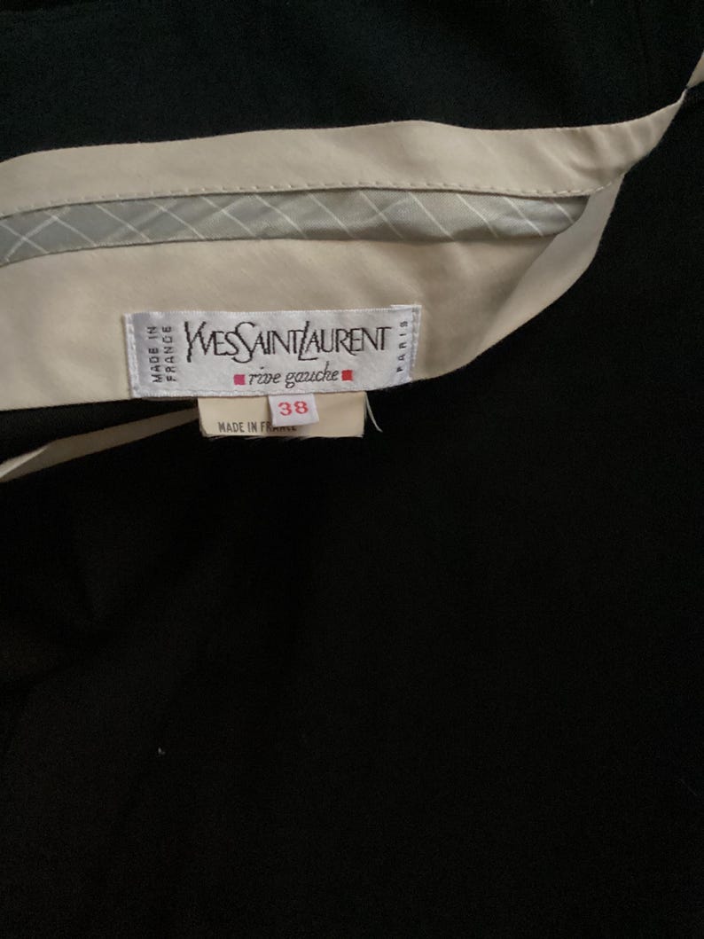 Puede incluir: Una etiqueta blanca con texto negro que dice "Yves Saint Laurent rive gauche" y "Made in France" con una etiqueta de talla 38.