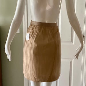May include: A tan-colored skirt with a gathered, bubble-like silhouette. The skirt has a fitted waistband and a soft, flowing fabric. A tag is attached to the skirt. The skirt is displayed on a mannequin.