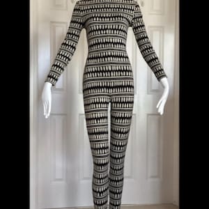 May include: A long-sleeved, full-length jumpsuit featuring a black turtleneck collar and a repeating pattern of vertical white dashes on a black background. The garment is fitted, covering the torso, arms, and legs down to the ankles.