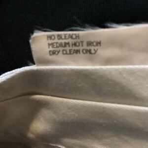 Puede incluir: Primer plano de una etiqueta de cuidado de la tela blanca con el texto "NO BLEACH MEDIUM HOT IRON DRY CLEAN ONLY".