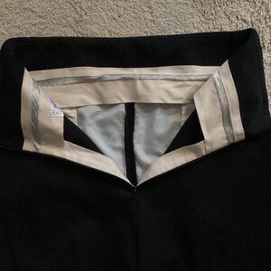 Puede incluir: Pantal&oacute;n negro con cintura blanca y una banda plateada. La cintura tiene una etiqueta blanca con texto negro.