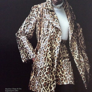 Puede incluir: Una mujer lleva un abrigo y una minifalda a juego con estampado de leopardo. El abrigo tiene cierre de doble botonadura y un cuello grande. La falda es de línea A y llega por encima de la rodilla. El texto de la imagen dice: "Moschino Cheap & Chic separaciones de algodón con estampado de leopardo: Abrigo, 915,00 €. Minifalda, 180,00 €. Ambos importados; disponibles en Designer Sportswear en tiendas selectas."