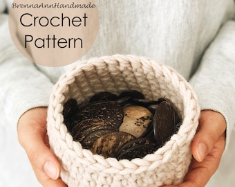May include: A close-up of a crocheted basket in a light beige colour, held by hands. The basket is filled with small, round, brown objects.