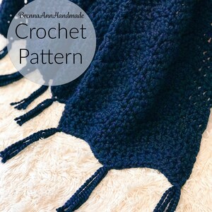 May include: A navy blue crochet blanket with fringe on the edges. The blanket is on a white fluffy surface. The text "BrennaAnnHandmade Crochet Pattern" is visible in the top left corner of the image.