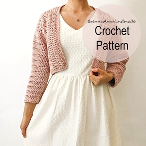 May include: A pink crochet shrug with long sleeves and a V-neck. The shrug is worn over a white dress. The text "BrennaAnnHandmade Crochet Pattern" is superimposed on the image.