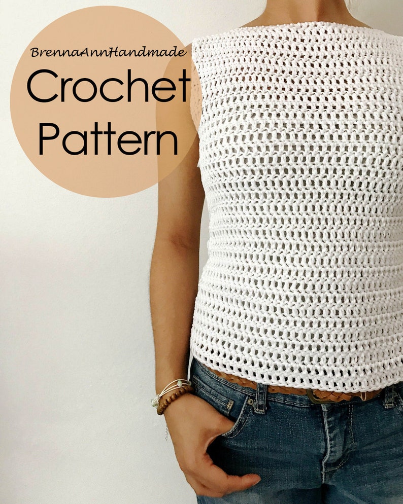 K&ouml;nnte beinhalten: Wei&szlig;es H&auml;keltop mit einem lockeren, offenen Muster. Das Top hat einen Boot Ausschnitt und ist &auml;rmellos. Das Model tr&auml;gt das Top mit einem braunen G&uuml;rtel und einer blauen Jeans.