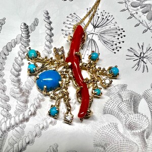 May include: A gold pendant necklace with a coral branch and turquoise stones. The pendant is shaped like a tree branch with a coral branch in the center. The pendant is surrounded by turquoise stones.