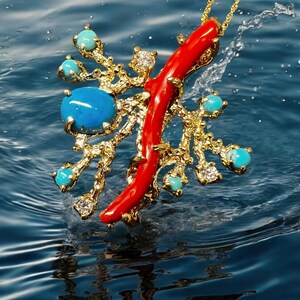 May include: A gold pendant necklace with a red coral branch and turquoise gemstones. The pendant is shaped like a tree branch with a red coral branch extending from the center. The pendant is hanging from a gold chain and is suspended in the air above a blue water surface.