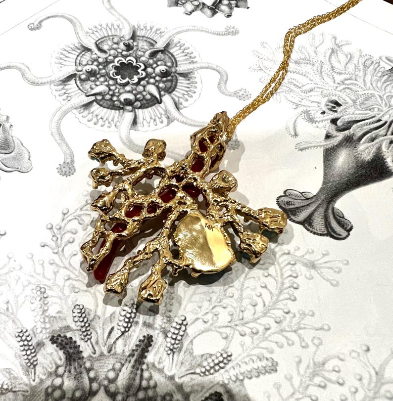 May include: A gold pendant necklace with a red and gold coral-like design. The pendant is marked "14K" on the back.