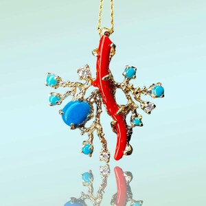 May include: A gold necklace with a pendant featuring a red coral branch and turquoise stones. The pendant is designed to resemble a coral reef.