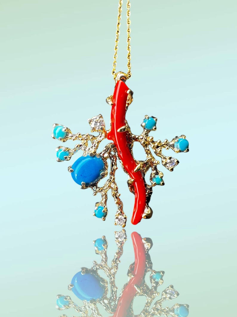 May include: A gold necklace with a pendant featuring a red coral branch and turquoise stones. The pendant is designed to resemble a coral reef.