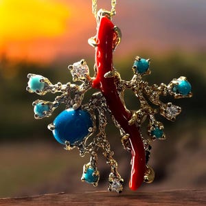 May include: A gold pendant necklace with a red coral branch and turquoise gemstones. The pendant is shaped like a tree with branches and leaves.