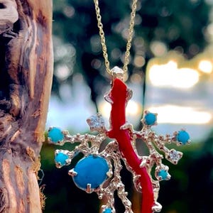 May include: A gold chain necklace with a pendant featuring a red coral branch with turquoise and clear stones.