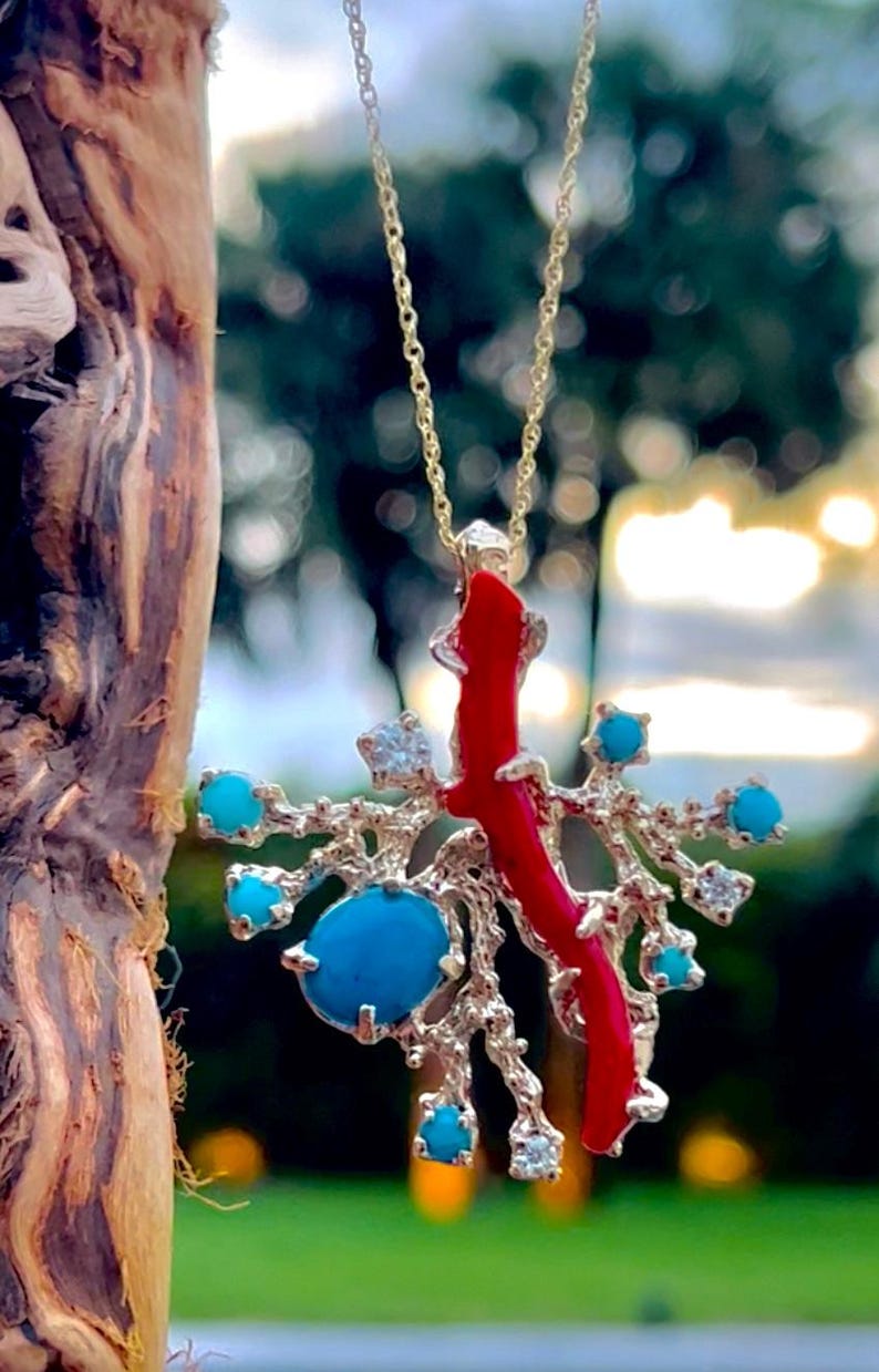 May include: A gold chain necklace with a pendant featuring a red coral branch with turquoise and clear stones.