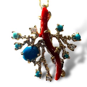 May include: A gold necklace with a pendant featuring a red coral branch and turquoise stones. The pendant is shaped like a tree branch with a coral branch extending from the top. The pendant is surrounded by turquoise stones.