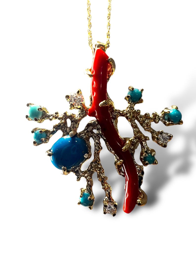 May include: A gold necklace with a pendant featuring a red coral branch and turquoise stones. The pendant is shaped like a tree branch with a coral branch extending from the top. The pendant is surrounded by turquoise stones.