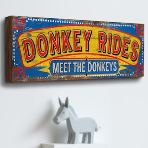 May include: A vintage-style wooden sign with blue, yellow and red paint. The sign reads "Donkey Rides Meet the Donkeys".