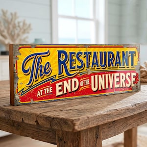 May include: A rectangular wooden sign with a distressed finish featuring a yellow background with blue and red text that reads The Restaurant at the End of the Universe. The sign has a weathered appearance with visible cracks and worn edges.