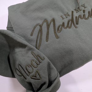 May include: A green hooded sweatshirt with the text "In My Madness" embroidered on the front and "Noah" embroidered on the sleeve.