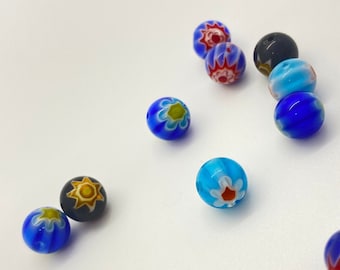 May include: Assortment of colorful glass beads with floral patterns. The beads are blue, black, and turquoise with white and yellow accents.