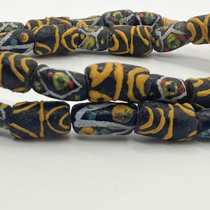 Può includere: Una collana di perline di vetro nero con motivi geometrici gialli e bianchi. Le perline sono infilate su un cordoncino e sono disposte in ordine casuale.