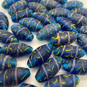 May include: A collection of blue glass beads with yellow and white swirl designs. The beads are oval shaped and have a frosted finish.