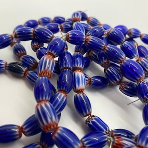 May include: A strand of blue and white striped glass beads with red accents. The beads are oval shaped and have a glossy finish.