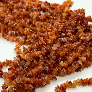 May include: A strand of carnelian chip beads. The beads are a deep orange colour and have a natural, irregular shape. They are strung on a clear thread.