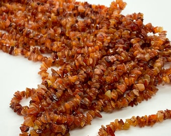 May include: A strand of carnelian chip beads. The beads are a deep orange color and have a natural, irregular shape. They are strung on a clear thread.