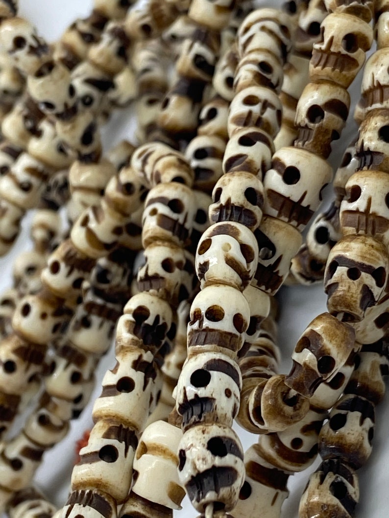 May include: A strand of white bone beads shaped like skulls. The beads are strung together with a dark brown cord.