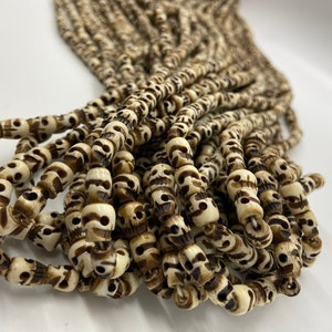 May include: A strand of white and brown skull beads. The beads are made of bone and have a carved skull design.